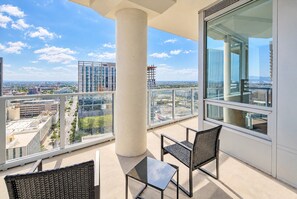 A balcony with a table and chairs, large windows, and a view of the cityscape.