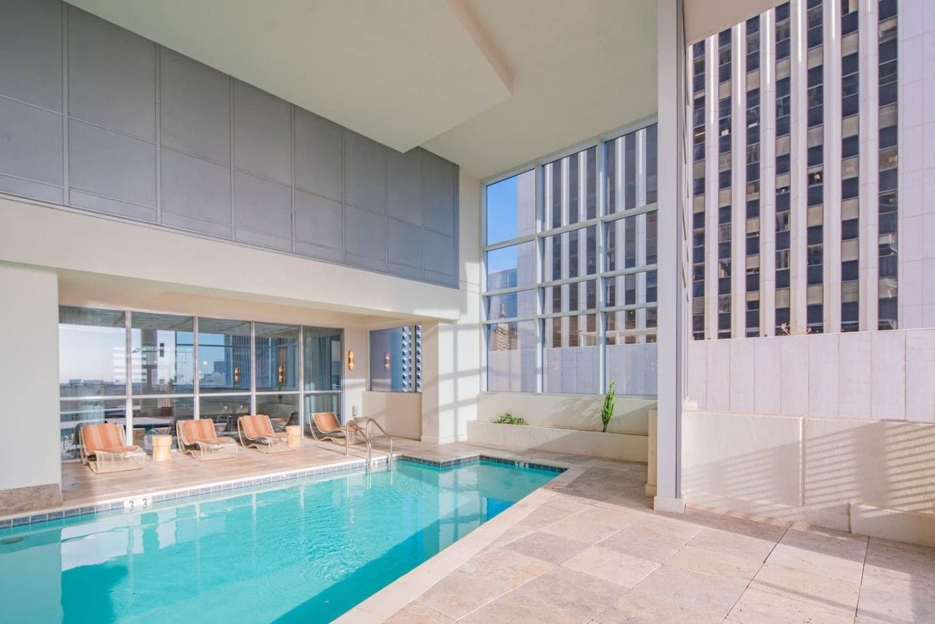 An indoor swimming pool with lounge chairs and a view of a cityscape.