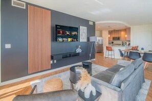 A modern living room with a large flat-screen TV, a sofa, a coffee table, and a decorative vase. - Modern HighRise Sanctuary+Gym+Pool+Prking+W/D (Phoenix)