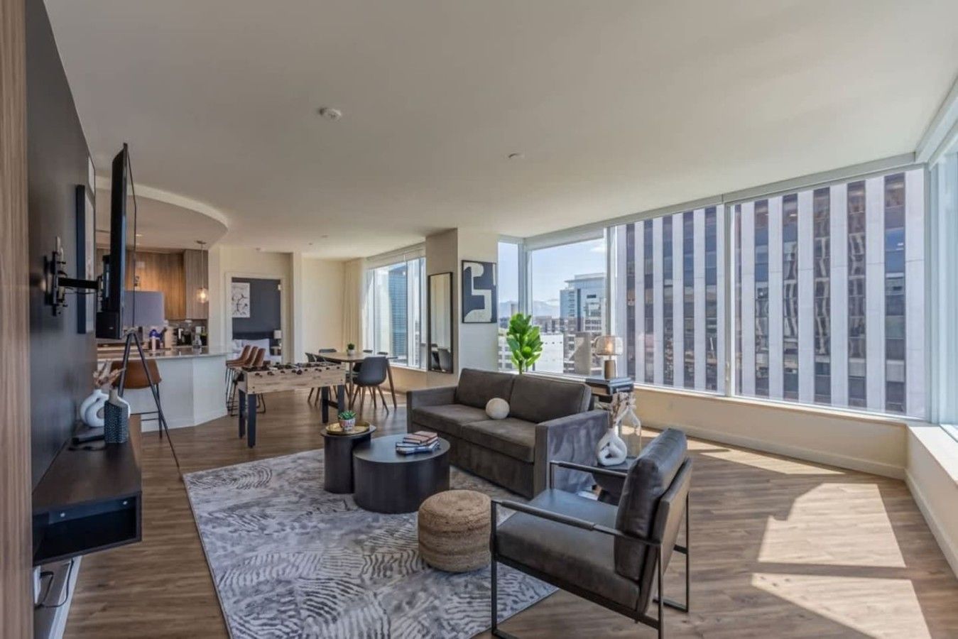 Un salon moderne avec un canapé, une table basse et une vue sur la ville grâce à de grandes fenêtres.