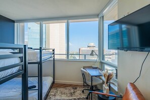 A hotel room with bunk beds, a desk, a chair, a TV, and a large window with a city view.