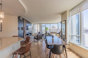 A modern living room with a large window, a dining area with a table and chairs, and a seating area with sofas and a coffee table.