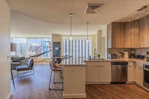 Une cuisine moderne dotée d’un îlot central, d’appareils électroménagers en acier inoxydable et offrant une vue sur la ville grâce à de grandes fenêtres.