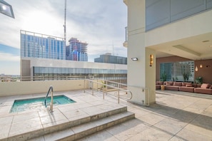 Un espace piscine sur le toit offrant une vue sur les gratte-ciel de la ville, un coin salon avec des canapés et un escalier menant à la piscine.