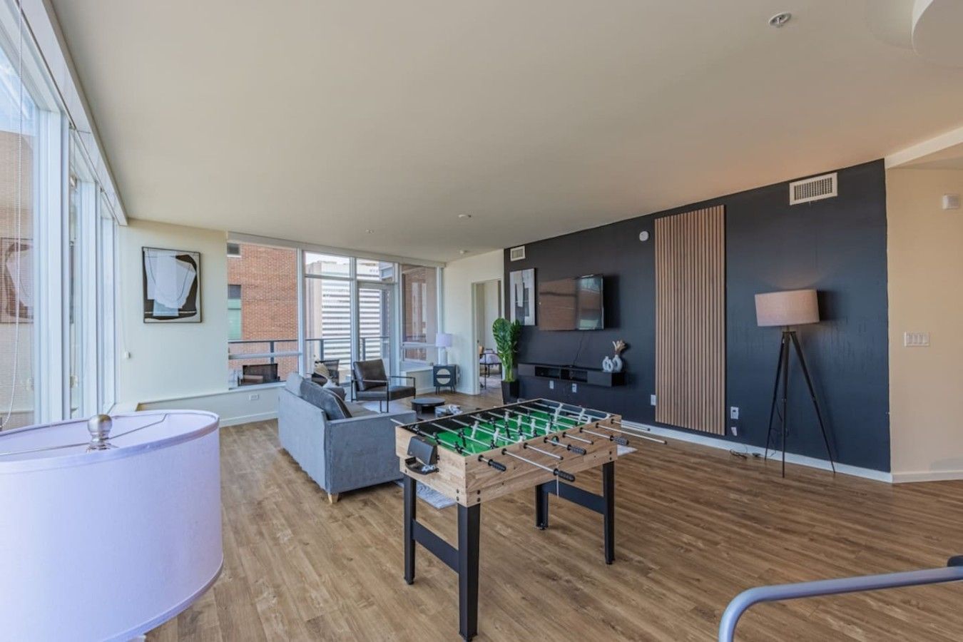A modern living room with a foosball table, a sofa, a TV, and a lamp.