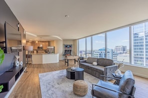 A modern apartment with a living room, kitchen, and large windows offering a city view. - Modern ASU Retreat | Pool | Gym | Balcony | W/D (Phoenix)