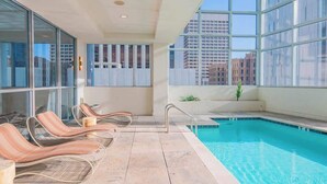 Un área de piscina interior moderna con sillas de descanso y vistas a edificios de la ciudad.
