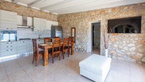 A modern kitchen with stone walls, a dining area with wooden chairs, and a white sofa.