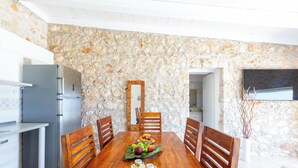 A dining area with a stone wall, wooden table, chairs, and a fruit bowl.