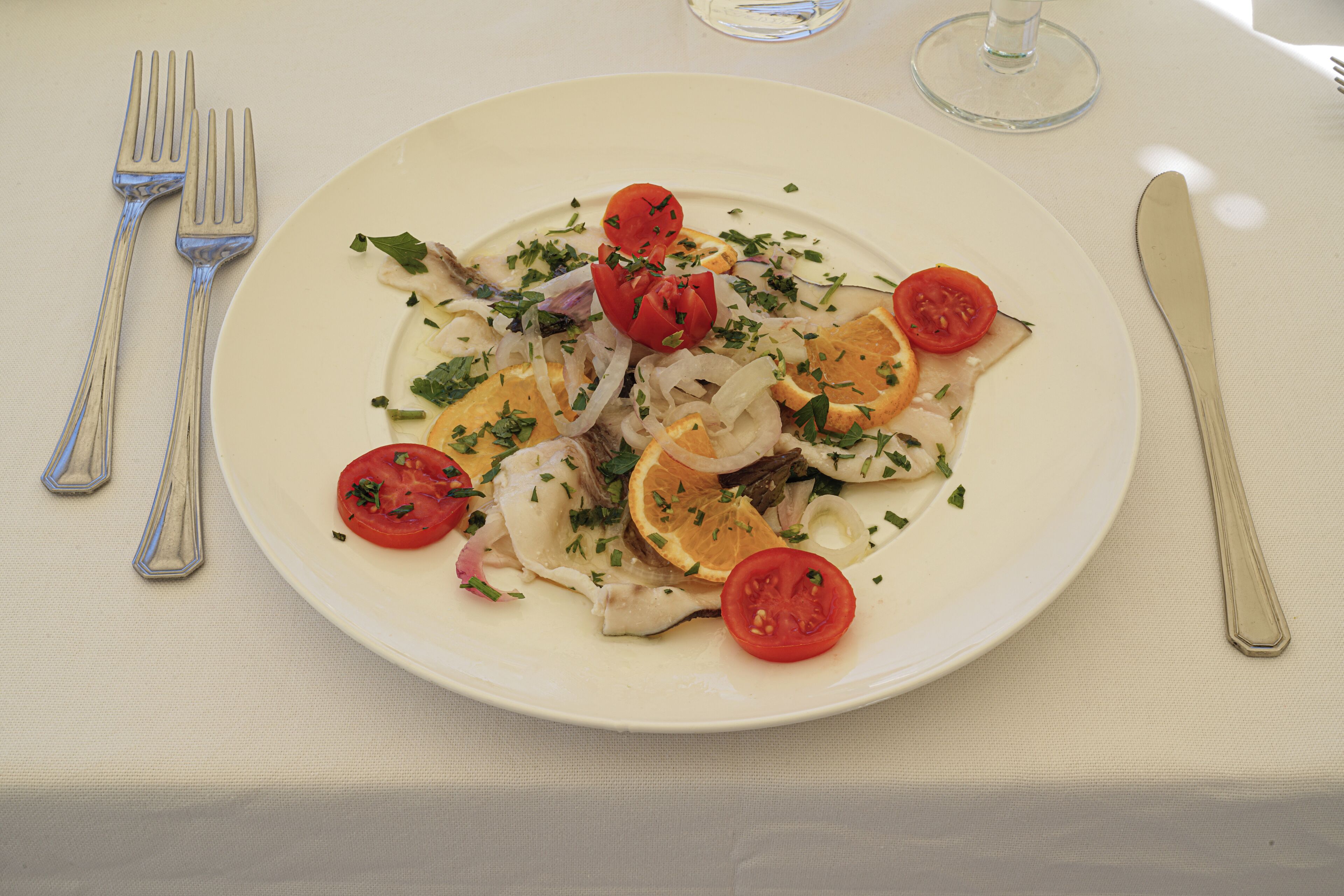 A plate of food with tomatoes, onions, and herbs on a white tablecloth.