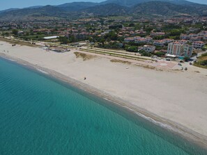 An aerial view of a coastal town with a beach, buildings, and mountains in the background.