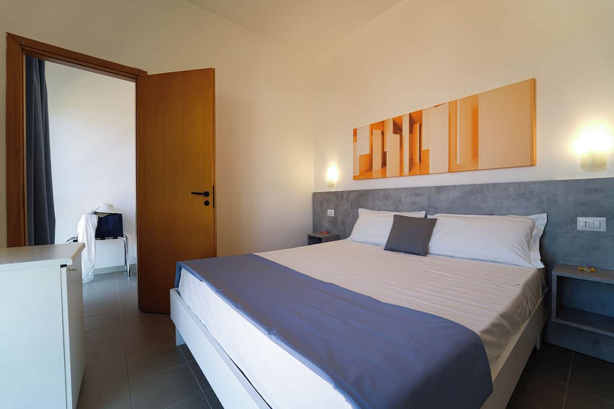A modern hotel room with a large bed, a desk, and a wardrobe.