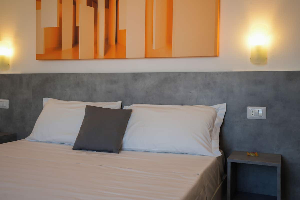 A neatly made bed with white and gray linens, a gray headboard, and two wall-mounted light fixtures.