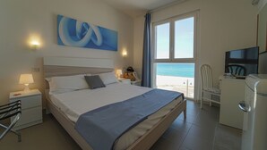 A hotel room with a bed, a desk, a chair, a TV, and a window with a view of the beach. - Hotel Rivabella (Davoli)