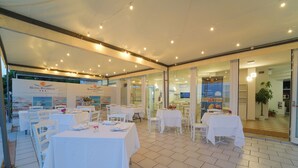 A restaurant with white tables and chairs, a tiled floor, and a glass wall. - Hotel Rivabella (Davoli)