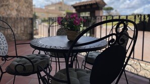 A patio with a round table and four chairs, a potted plant with flowers, and a stone wall in the background. - Casa Rural LA Divisa Hay Lugares Donde uno se Queda y Lugares que Quedan en uno (Boceguillas)