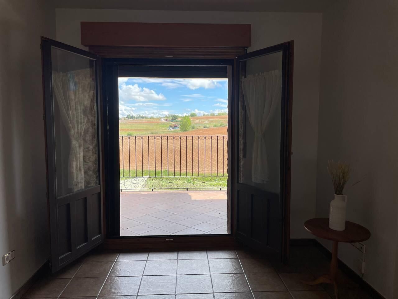 Puerta abierta que da a un patio con vista a un área cercada y un cielo despejado.