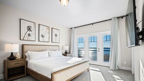 Een slaapkamer met een groot bed, twee nachtkastjes en uitzicht op het water door de glazen deuren.