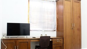 Un dormitorio con un escritorio de madera, una silla, un televisor y un armario.