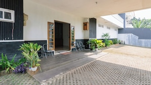 Un espacio al aire libre cubierto, con suelo de baldosas, una puerta de madera y plantas en macetas.