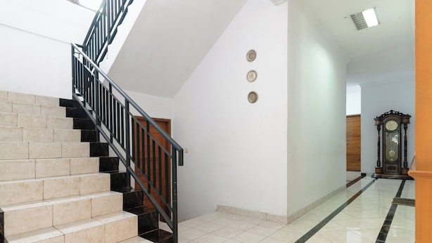 Una escalera con barandillas negras y baldosas color crema, que lleva a un cuarto con una puerta de madera y un reloj grande en la pared.