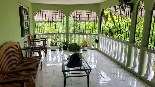 A covered balcony with a tiled floor, wooden furniture, potted plants, and a view of lush greenery. - Sun Valley Retreat in Montego Bay (Montego Bay)