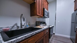 A kitchen with a black sink, wooden cabinets, a microwave, and a stainless steel refrigerator. - Dual patios, Free Laundry Service, College steps, 2BR 1 BA (Atchison)