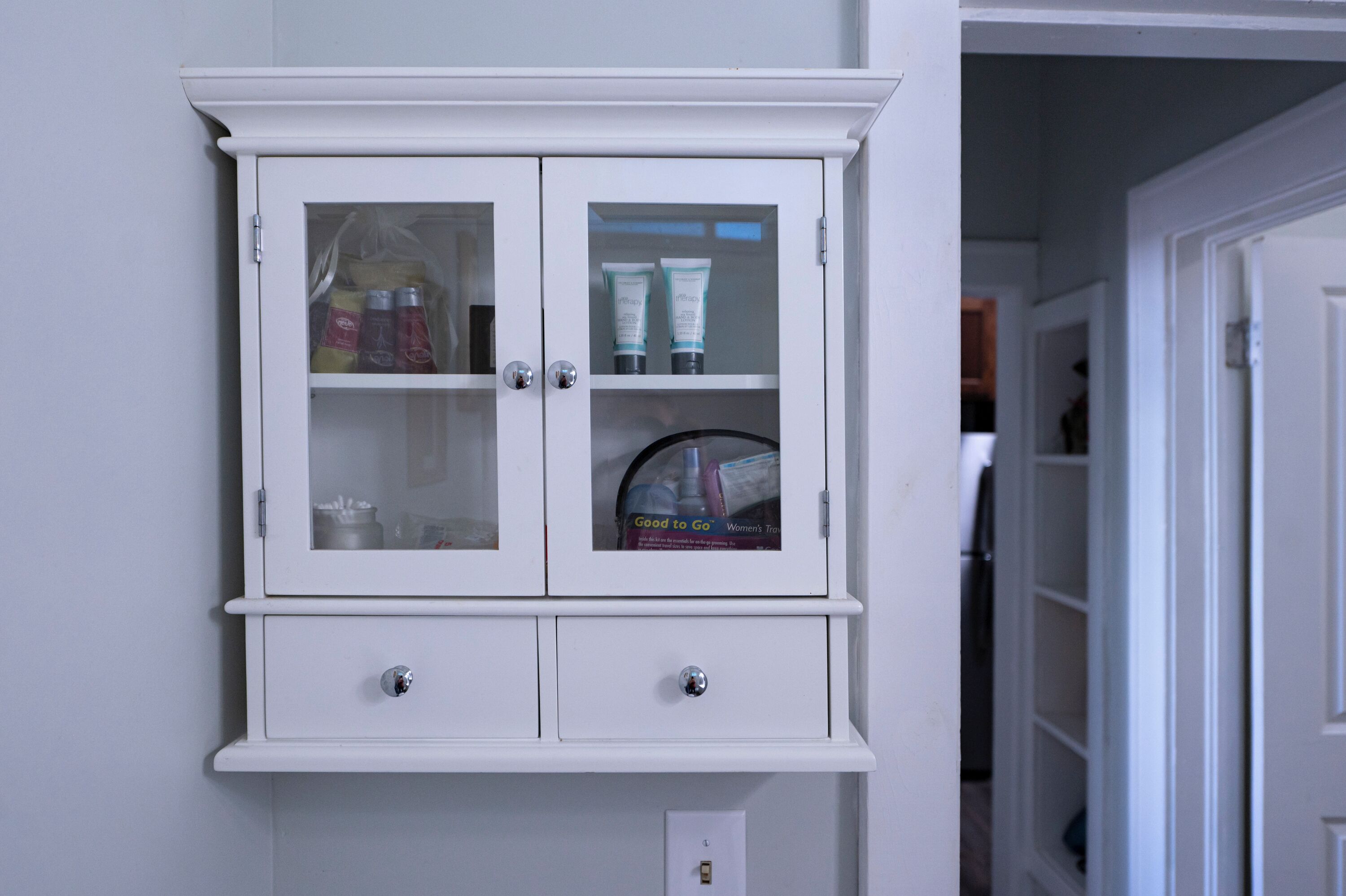 A white cabinet with glass doors containing toiletries.