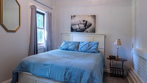 A bedroom with a bed, a nightstand, a lamp, a clock, and a framed picture on the wall. - Dual patios, Free Laundry Service, College steps, 2BR 1 BA (Atchison)
