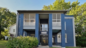 A two-story building with a balcony on the second floor, a front door, and a sign above the door. - Dual patios, Free Laundry Service, College steps, 2BR 1 BA (Atchison)
