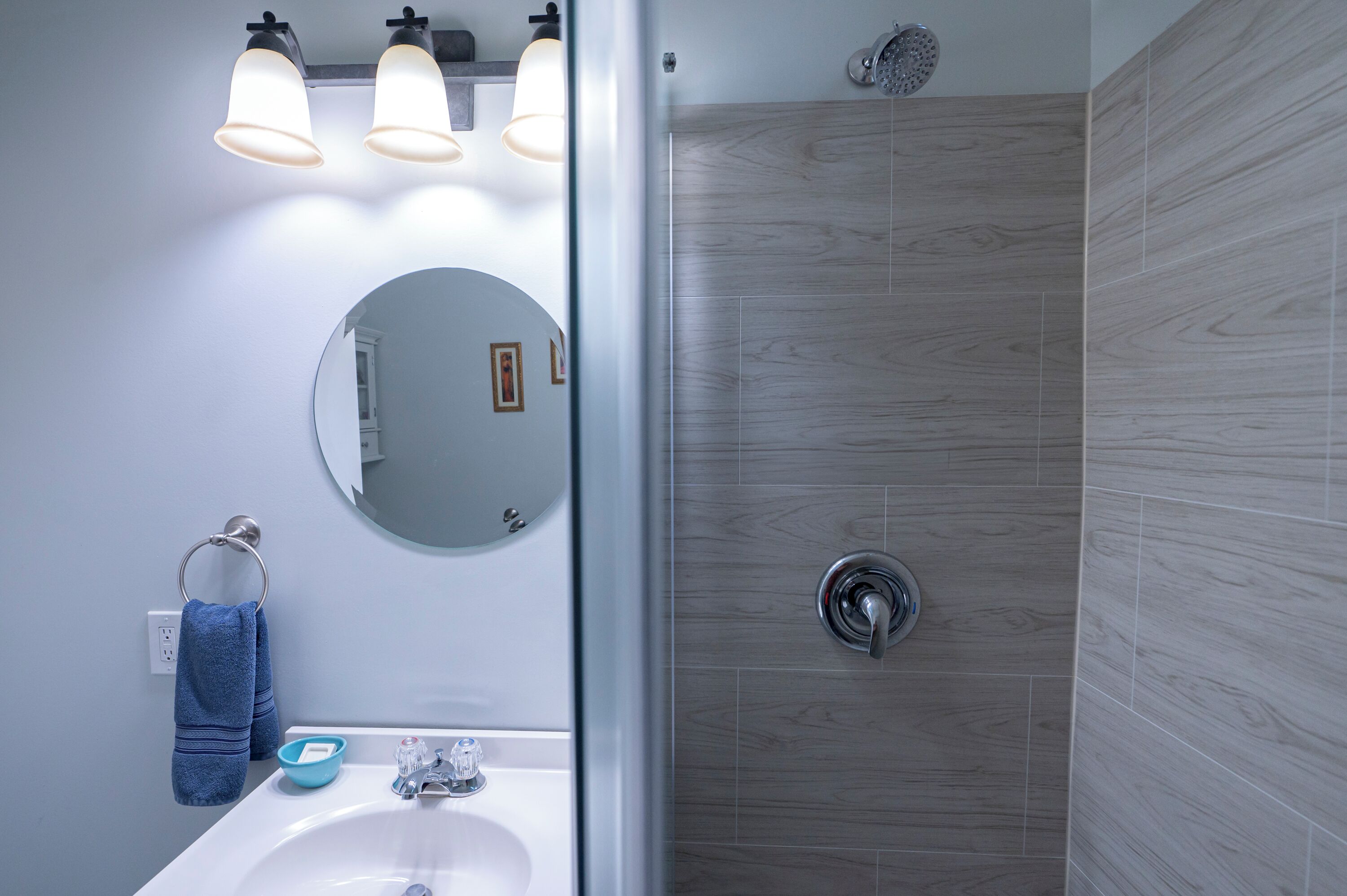 Ein Badezimmer mit Waschbecken, Spiegel, Handtuchhalter und Dusche mit Holzboden.