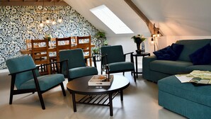 A cozy living room with a high ceiling, a skylight, and a patterned wall. There are several chairs and a sofa, with a table in the center. - Knus Landelijk Verblijf! (Alveringem)