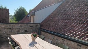 An outdoor patio with a wooden table and chairs, a vase with flowers, and a brick wall. - Knus Landelijk Verblijf! (Alveringem)