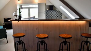 A modern kitchen with a wooden island and bar stools, a dining area with a table and chairs, and a view of the living room. - Knus Landelijk Verblijf! (Alveringem)