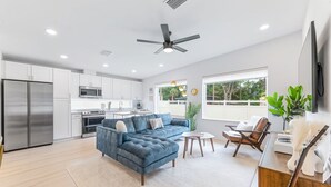 A modern kitchen with white cabinets, stainless steel appliances, and a blue sectional sofa.