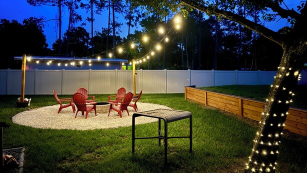 An outdoor patio area with a round table and red chairs, surrounded by a white fence and a wooden deck.