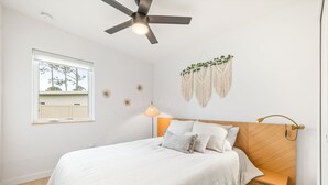 A neatly arranged bedroom with a bed, a ceiling fan, a window, and wall decorations.