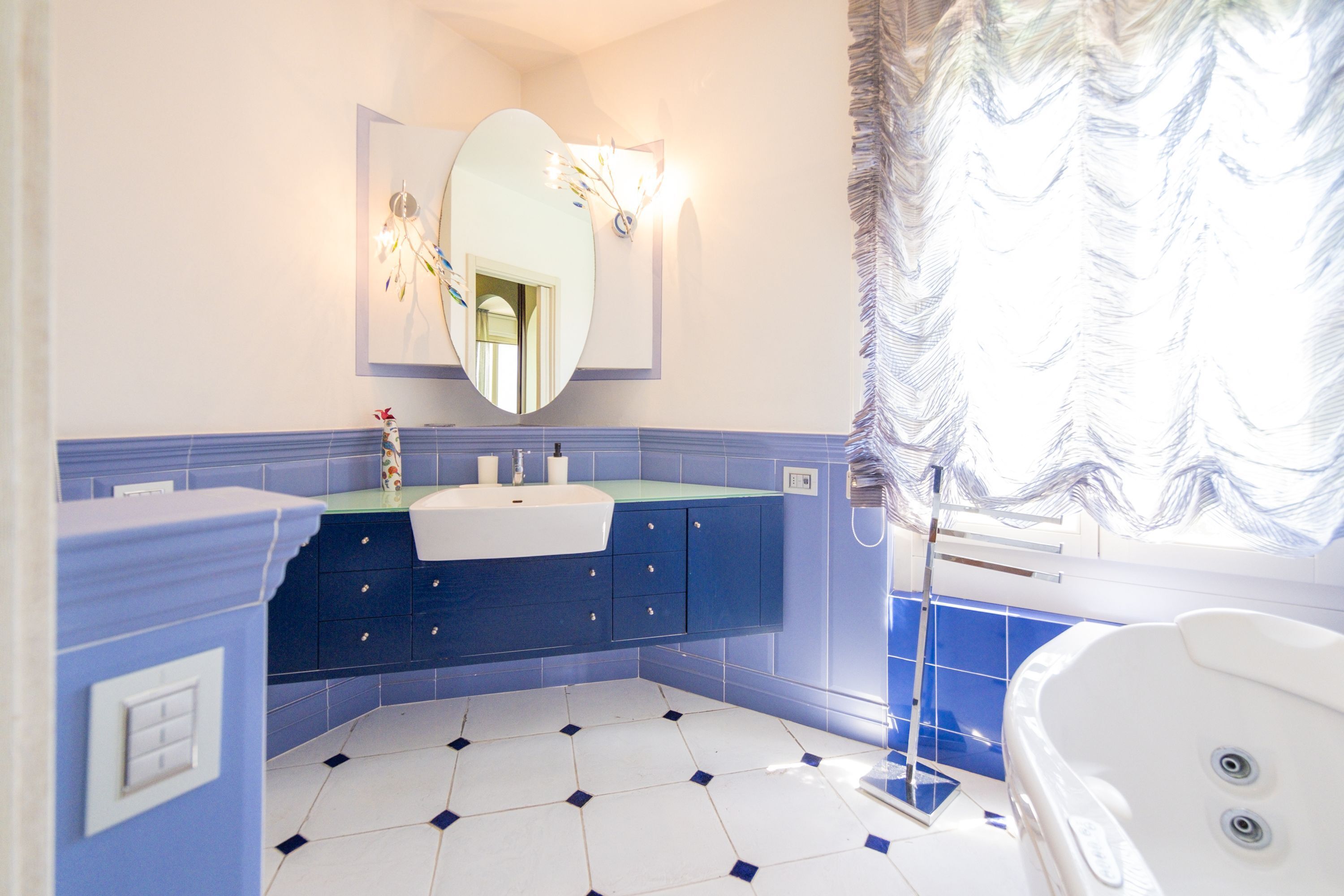 A bathroom with a white bathtub, a blue vanity with a mirror, and a white sink.