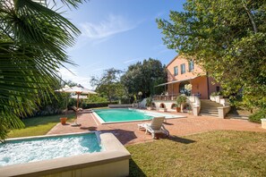 A swimming pool with a hot tub, a sun lounger, and a patio area with a staircase leading to a building.