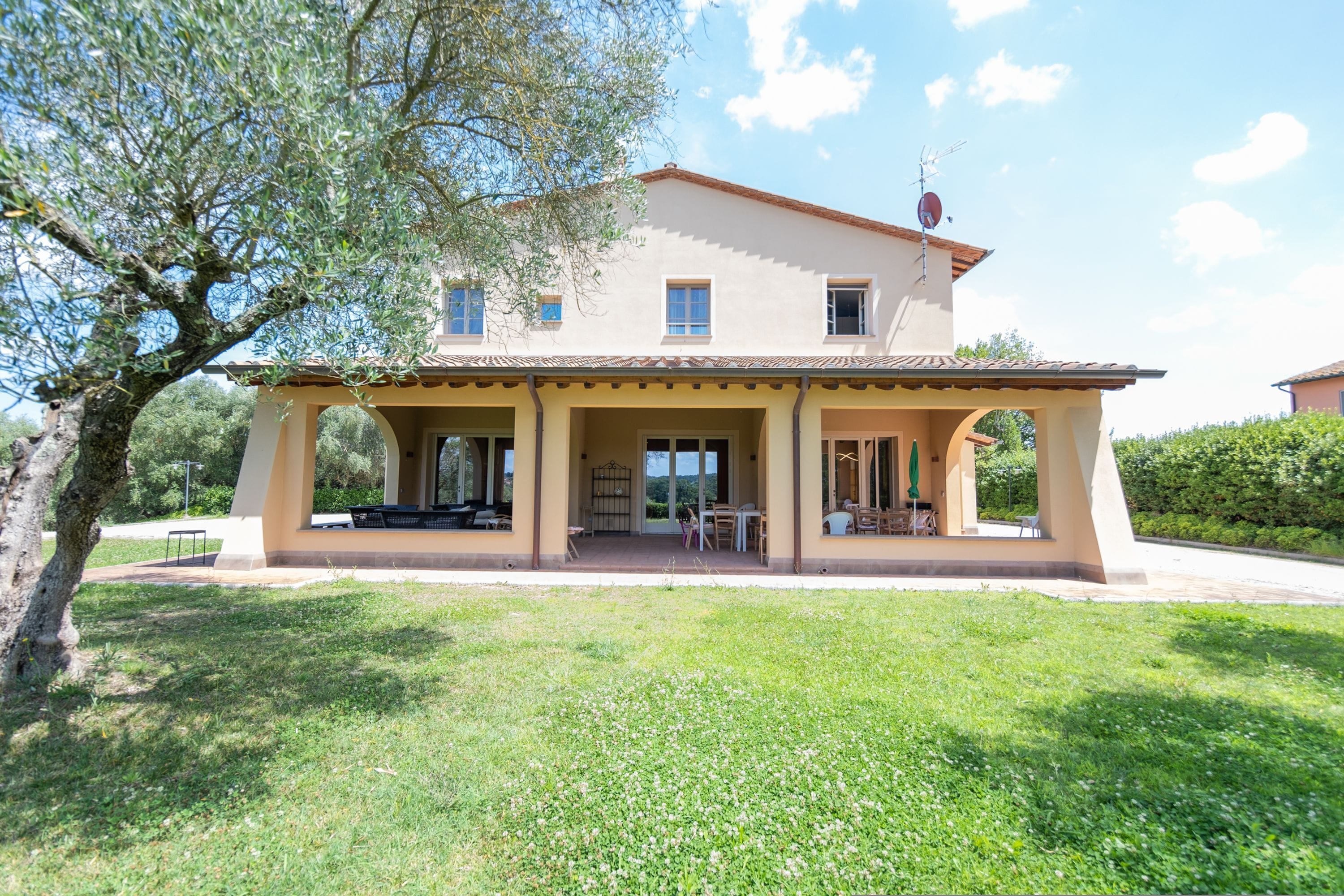 A two-story house with a covered patio, a large lawn, and a tree.