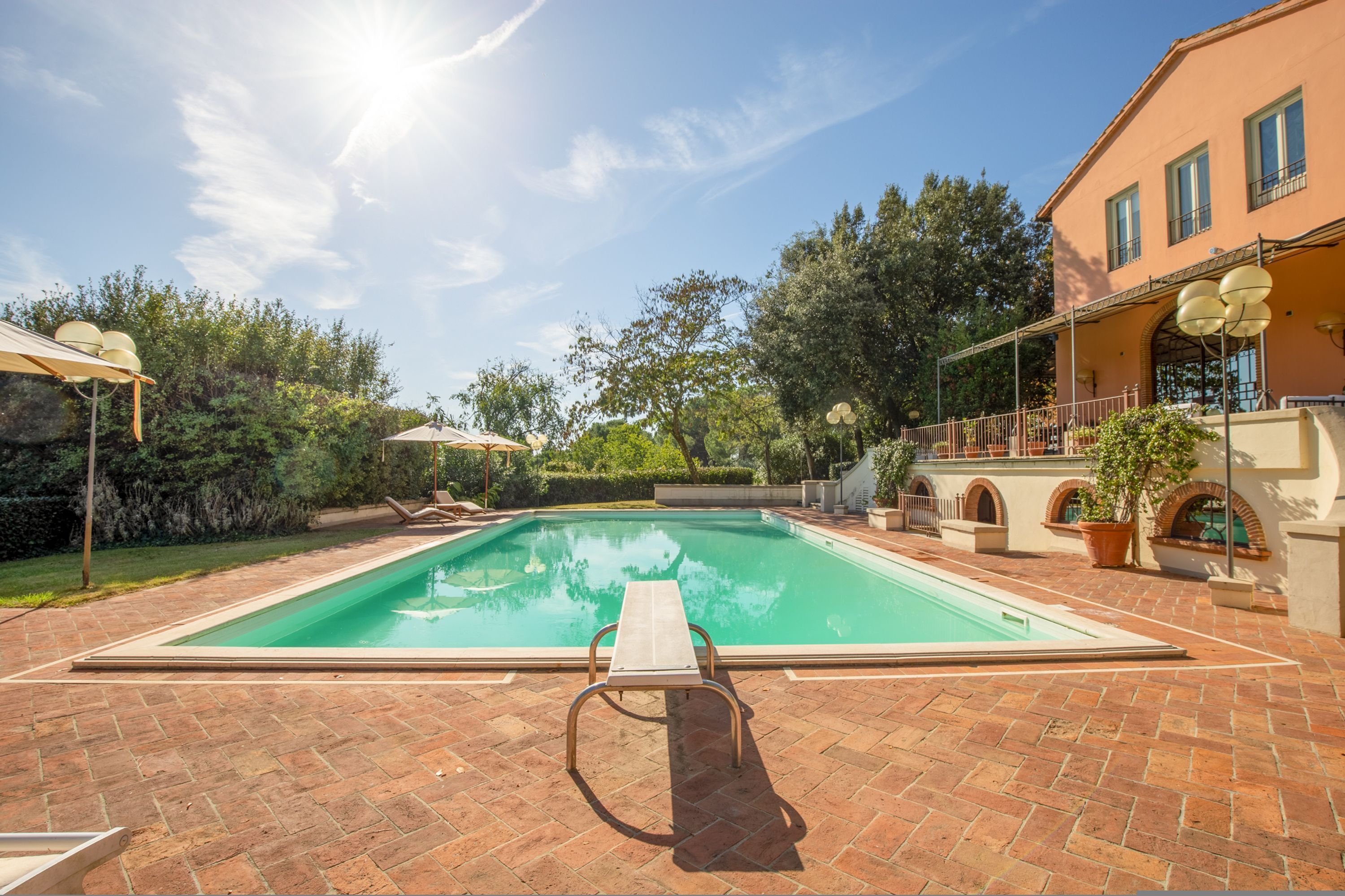 A rectangular swimming pool with a wooden deck in the foreground, surrounded by a brick patio.