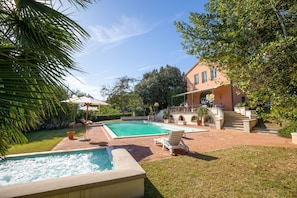 Una piscina con un jacuzzi, una tumbona y un patio con una escalera que lleva a un edificio.