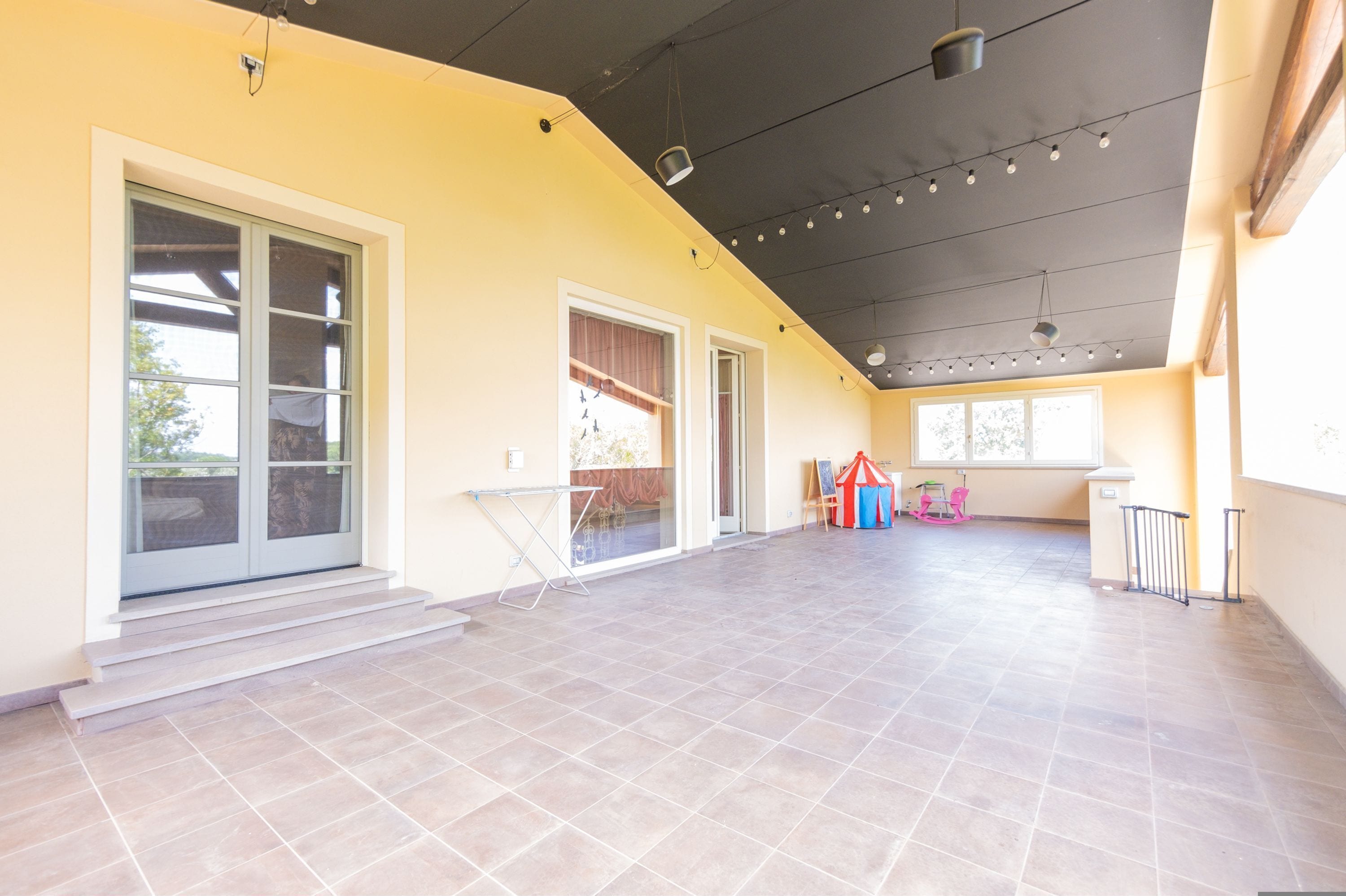 A spacious indoor area with a high ceiling, large windows, and a tiled floor.