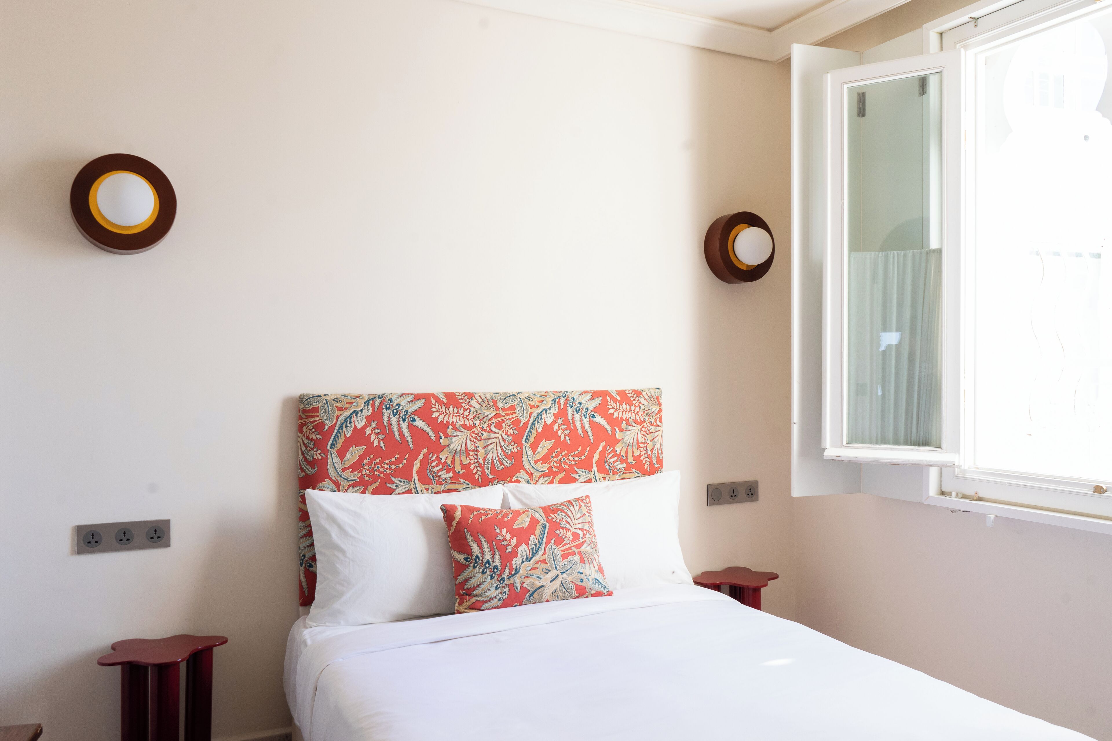 Un dormitorio con cama, ventana e enchufe.