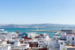 A coastal cityscape with a harbor, buildings with flat roofs, and a clear blue sky.