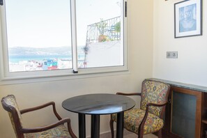 A room with a large window, two chairs, a small table, and a cabinet.