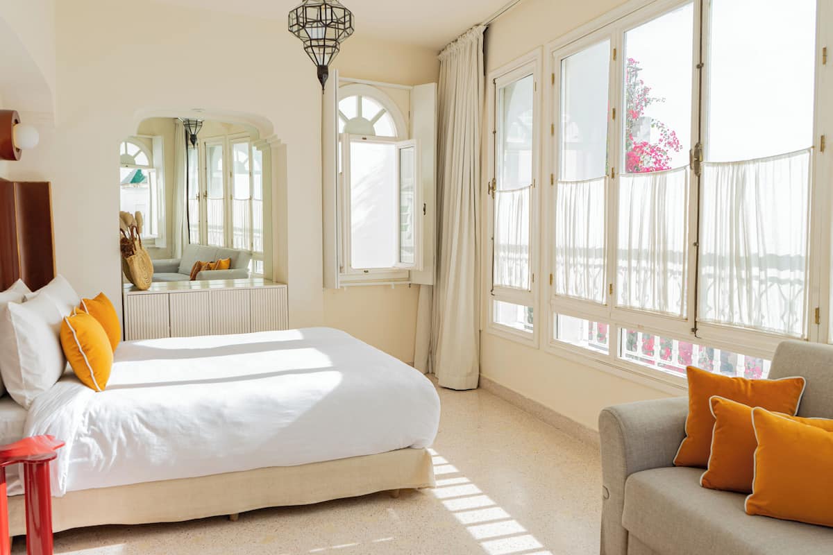 A bedroom with a bed, a sofa, and large windows.