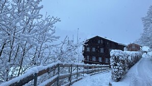 Un edificio cubierto de nieve con una valla de madera y árboles cargados de nieve.