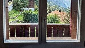 Vista desde un balcón con baranda de madera, sobre un paisaje montañoso con edificios y vegetación.