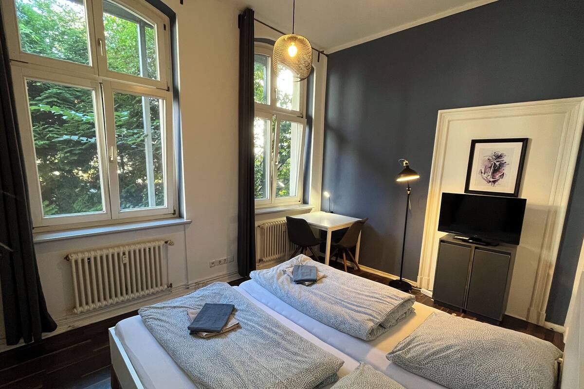 A bedroom with a bed, a desk, a TV, and a window with a view of trees.